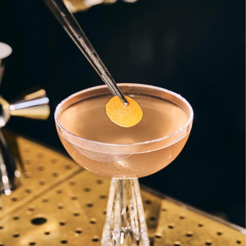 A tiny ten cocktail on a table being garnished.