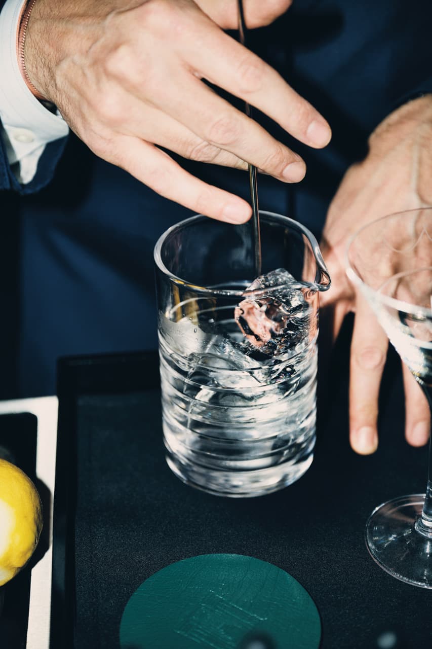 A cocktail is stirred with ice in a cocktail mixing glass.
