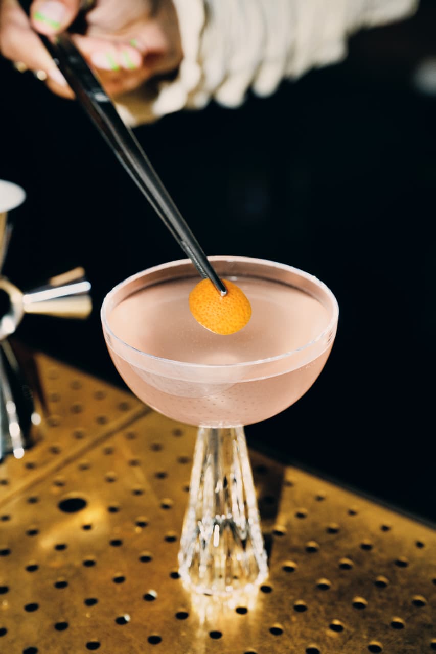 A tiny ten cocktail on a table being garnished.