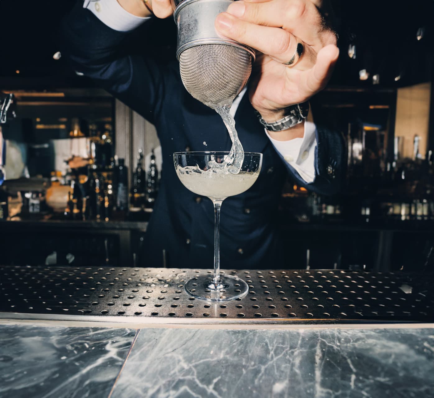 A hand straining a cocktail into a glass