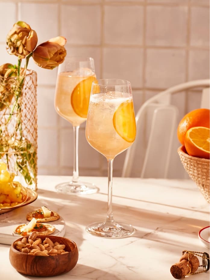 Two Tanqueray Flor de Sevilla 0.0 Spritz cocktails sitting on a table with a basket of oranges
