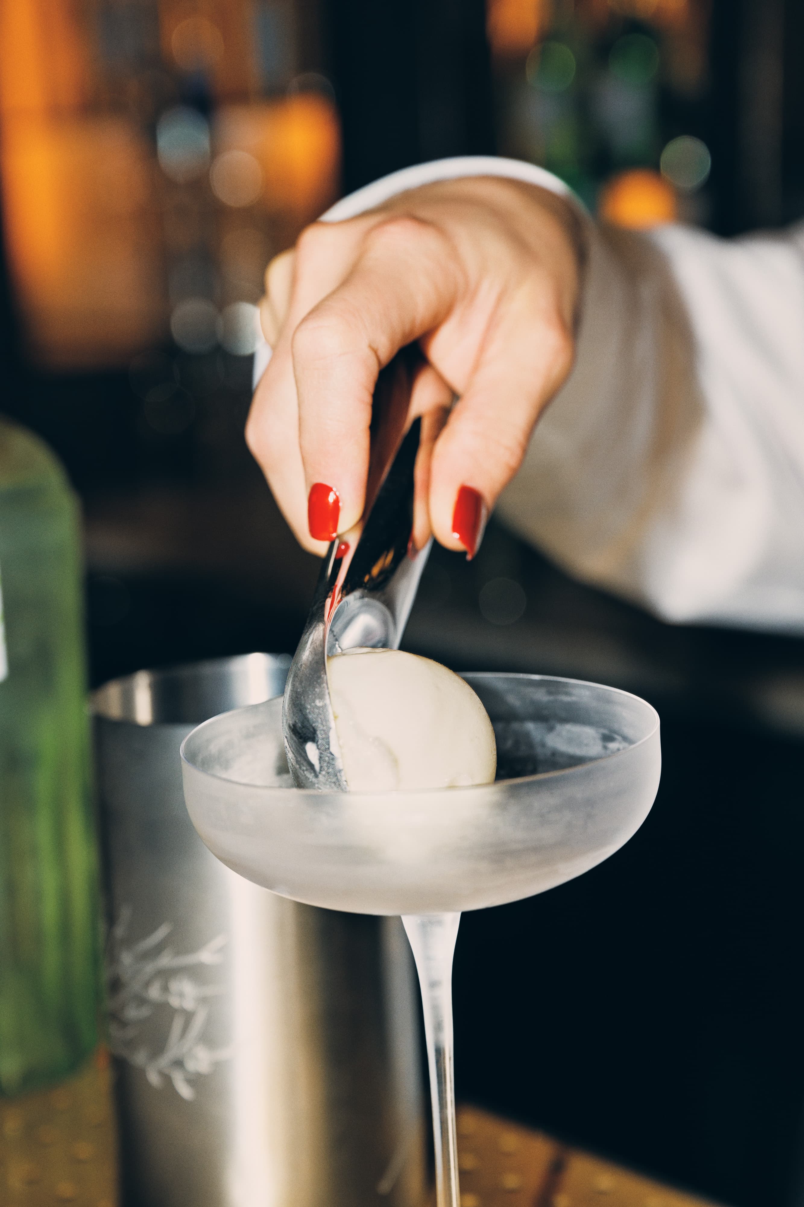 A hand is placing a scoop of lime sorbet into a chilled glass.