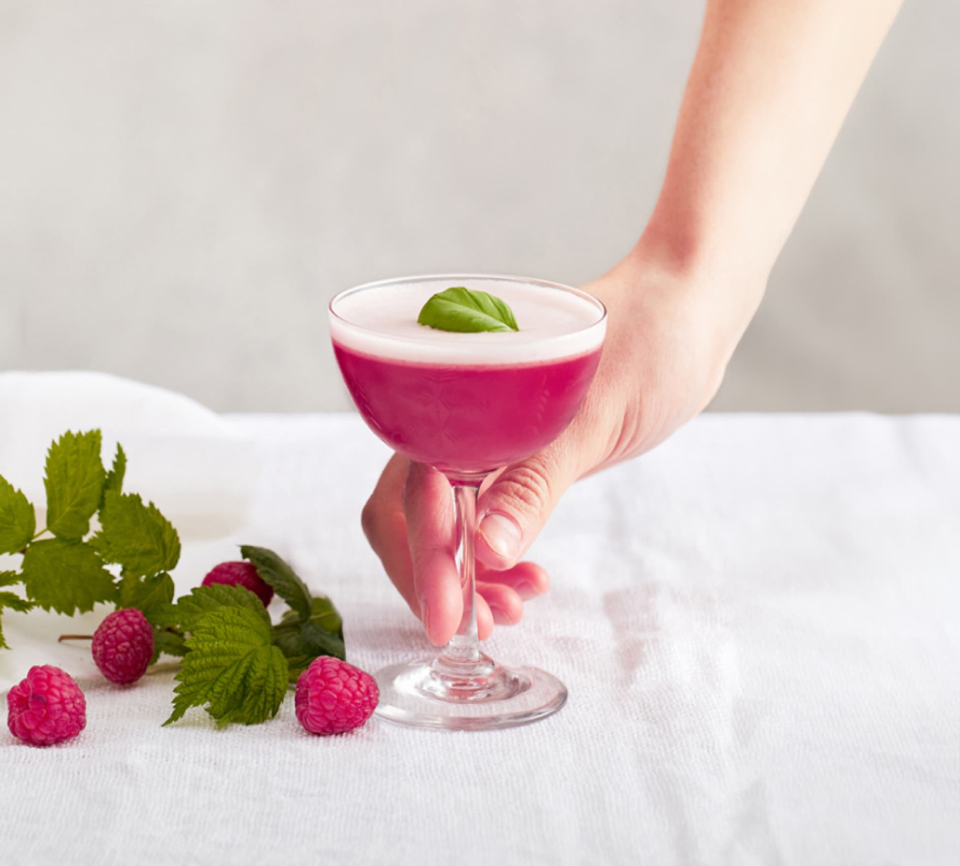 A bright pink cocktail with a hand grasping the stem of the cocktail glass.