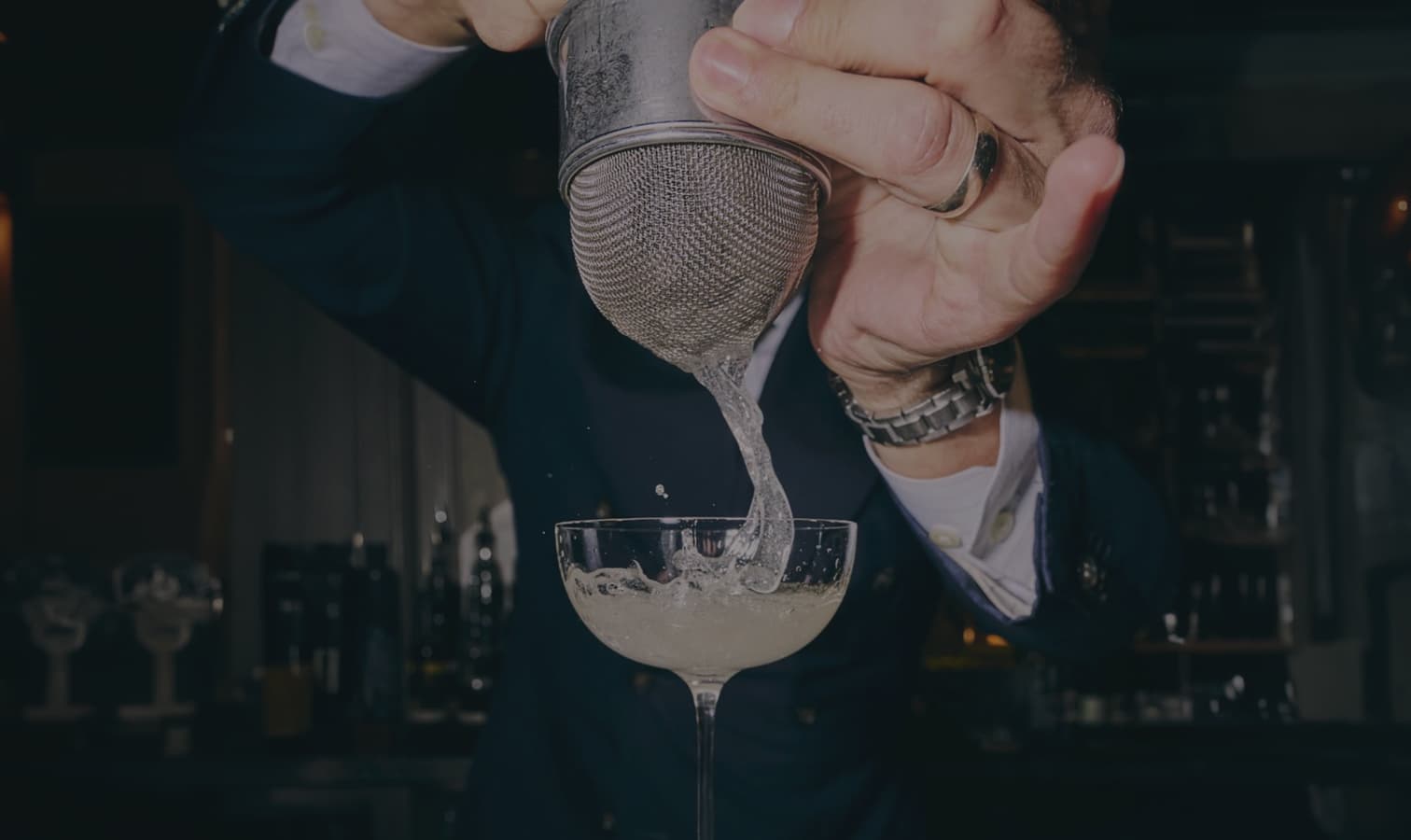 A hand straining a cocktail into a glass