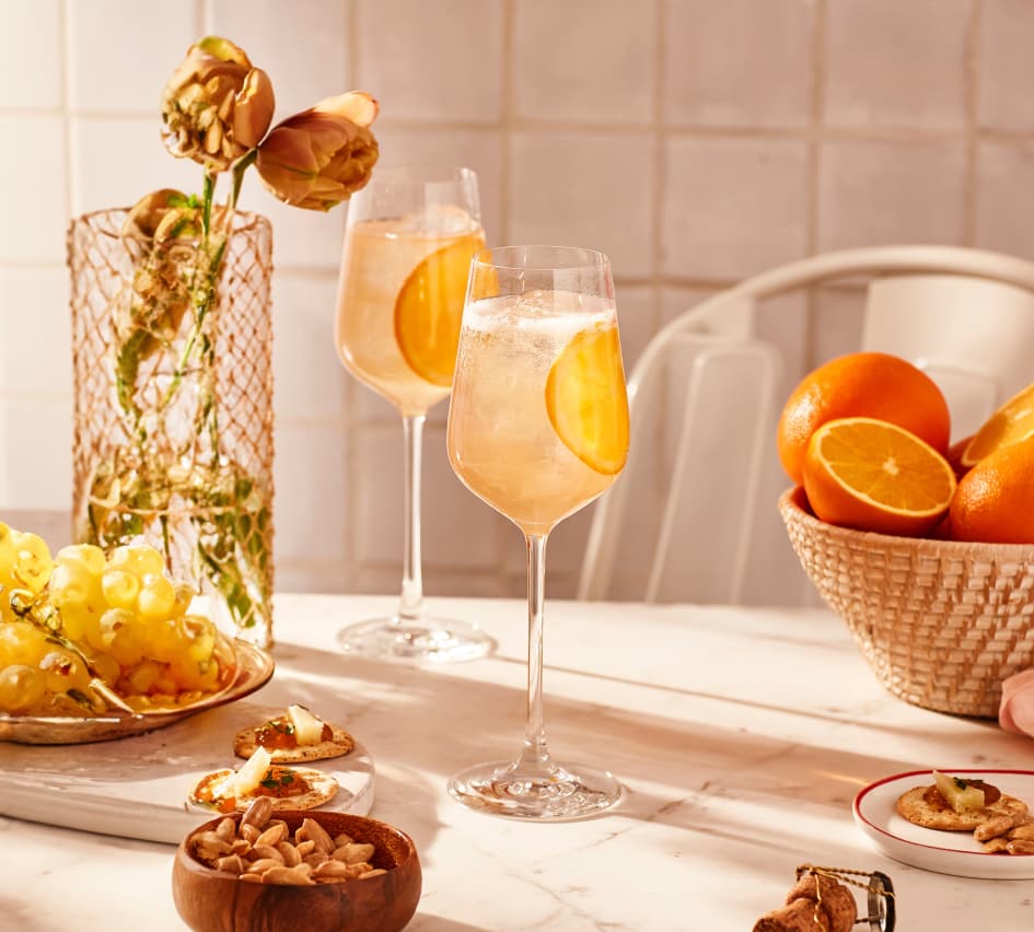 Two Sevilla Spritz cocktails sitting on a table surrounded by grapes, oranges, and other decorations.