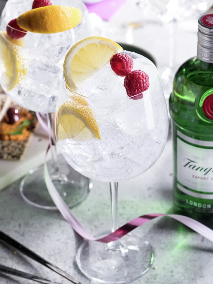 A Gin & Tonic cocktail made with Tanqueray London Dry Gin, garnished with lemons and raspberries