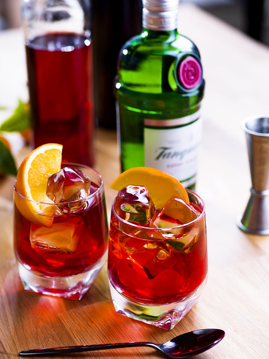 Two Negroni cocktails made with Tanqueray London Dry Gin on a table garnished with lemon slices