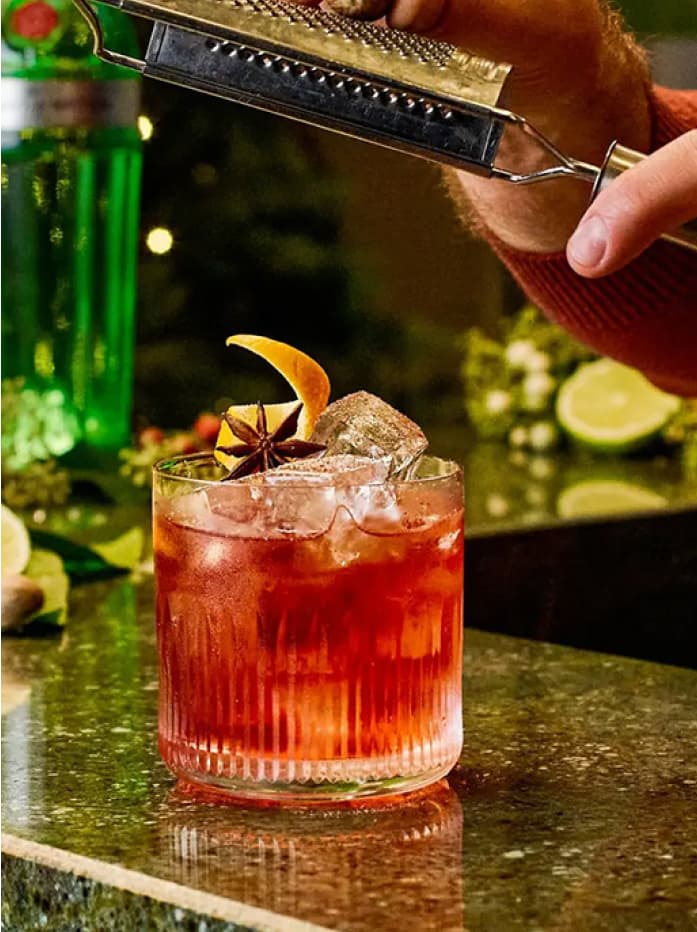 A Tanqueray Nº TEN Winter Spiced Negroni cocktail on a table garnished with an orange peel and a star anise
